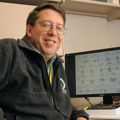 John Butler in his lab in front of a computer monitor with graphics on it